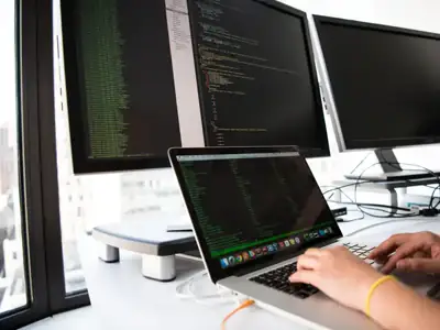 A laptop and two monitors full of source code, hands on the keyboard
