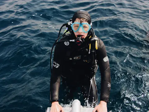 A scuba diver surfacing in open water, facing the camera