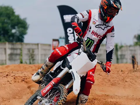 A motocross rider cornering on a dirt track, one leg out