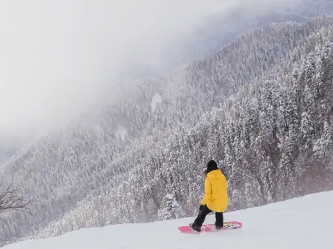 A snowboarder on an empty slope in falling snow and fog