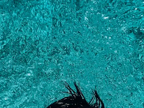 Split view of a swimmer, head underwater in turquoise water, back breaking the surface